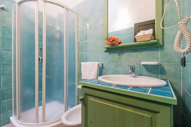 Bagno con doccia a vetri e piastrelle verdi.