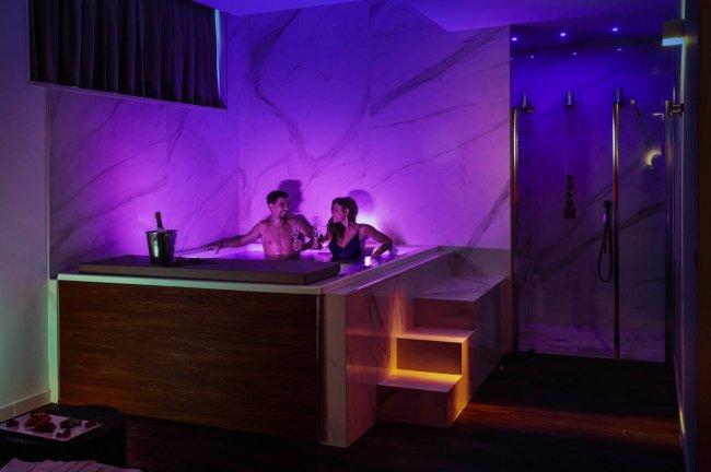 Vasca da bagno con luci soffuse viola e due persone.