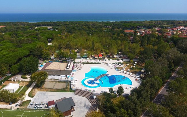 Piscina con scivolo circondata da verde e mare in lontananza.