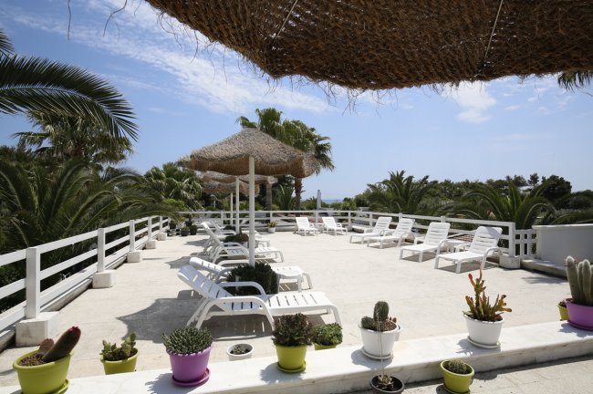 Terrazza con sdraio, piante e ombrelloni di paglia.
