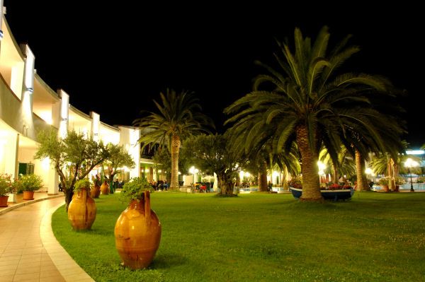 Giardino illuminato di notte con palme e vasi decorativi.
