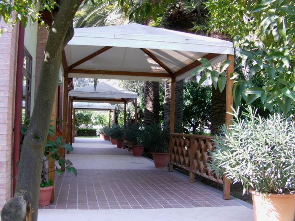Un viale coperto da pergole con vasi di piante ai lati, illuminato dal sole.
