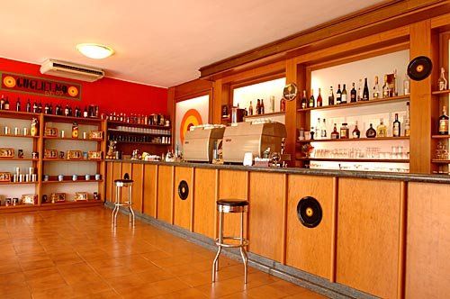 Interno di un bar con scaffali pieni di bottiglie e sgabelli di fronte al bancone.