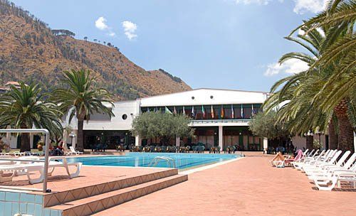 Piscina e lettini, con palme e montagne in lontananza.