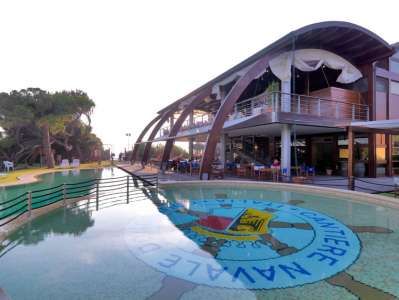 Edificio moderno con ampie vetrate, piscina con logo, e area pranzo esterna.