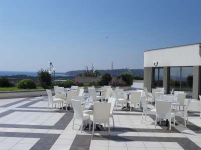 Una terrazza con tavoli e sedie bianche, vista mare e cielo sereno.