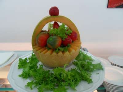 Un melone intagliato a forma di cestino con pomodori e insalata, su un vassoio bianco.