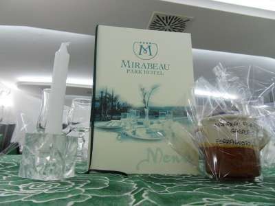 Menu del Mirabeau Park Hotel con candela e dolce confezionato su una tovaglia verde.