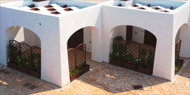 Cortile con archi bianchi, pareti intrecciate e piante in fioriere.