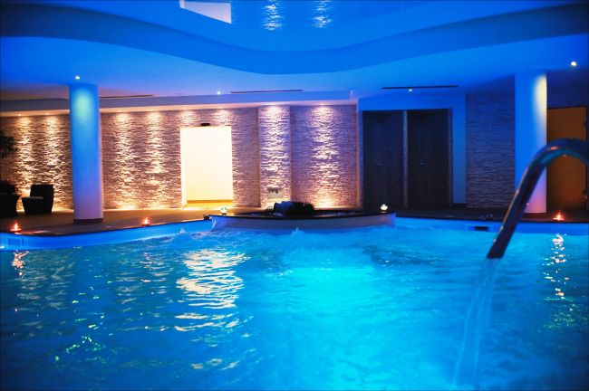 Piscina al coperto illuminata di blu, con pareti in pietra decorativa.