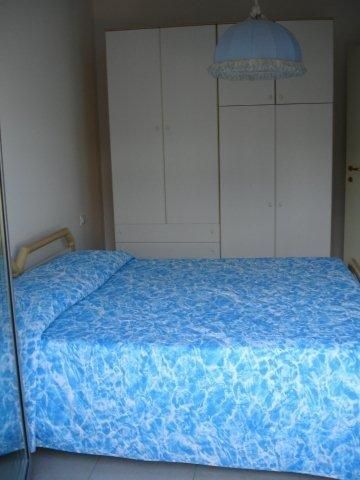 Camera da letto con letto matrimoniale coperto da trapunta blu e armadio bianco.