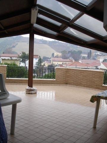 Una terrazza coperta con vista su colline e case in lontananza.