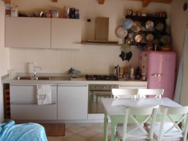 Cucina moderna con mobili chiari, tavolo con sedie e frigorifero rosa.