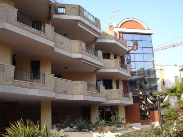 Edificio moderno con balconi in cemento e vetri riflettenti, circondato da piante.