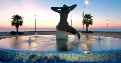 Fontana con una statua artistica al tramonto, circondata da palme.