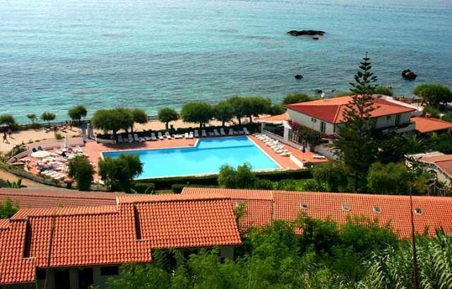 Piscina circondata da lettini, vicino a un edificio e al mare.