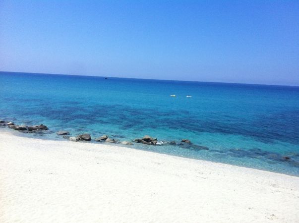 Spiaggia sabbiosa con acqua cristallina e rocce.