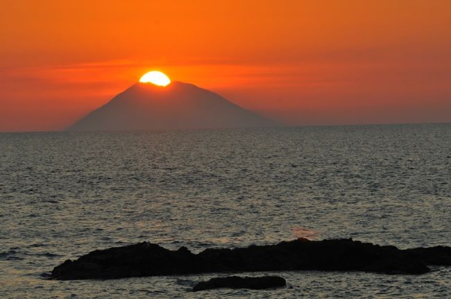 Tramonto sul mare con sole dietro un'isola.