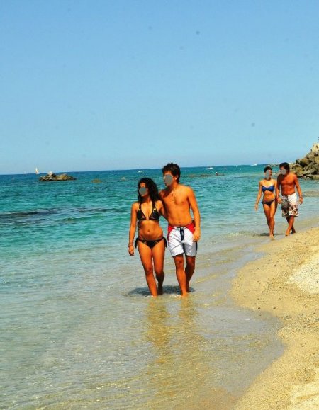 Coppia cammina sul bagnasciuga, mare limpido.
