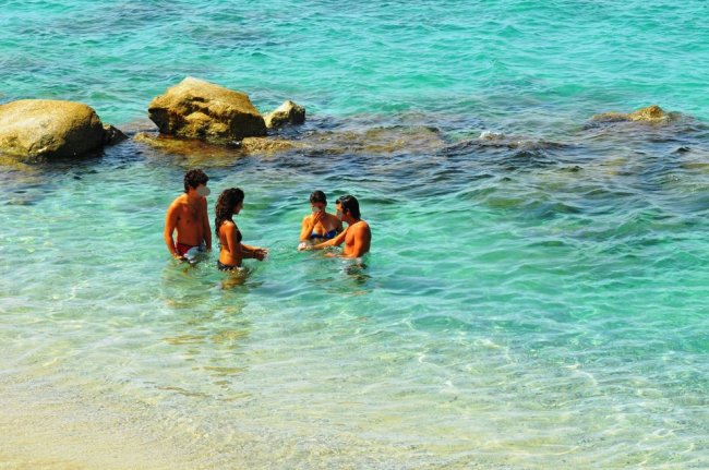 Quattro persone in acqua vicino a rocce.