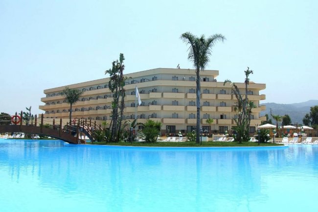 Ampia piscina davanti a un hotel con palme.