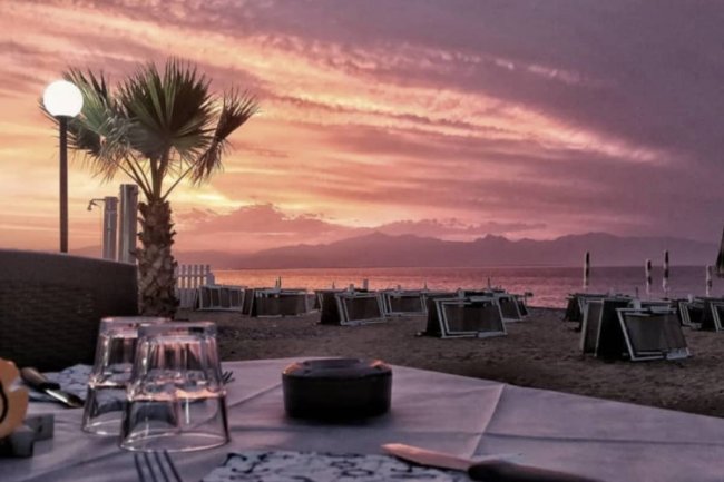 Tramonto sulla spiaggia con palme e ombrelloni.