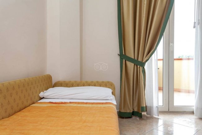 Letto singolo con coperta arancione, tende dorate.