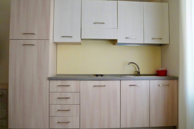 Cucina compatta chiara con pensili e lavello.