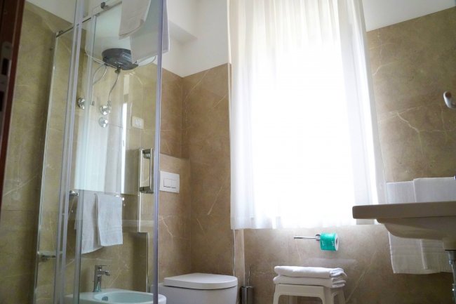 Bagno moderno con doccia in vetro, vaso, bidet e finestra.