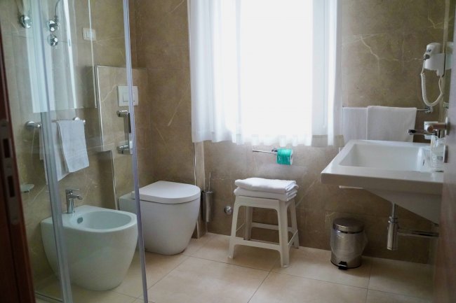 Bagno con lavabo, doccia, vaso e finestra con tenda.