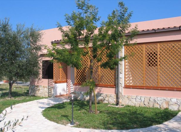 Edificio rosa con grata in legno e albero davanti.