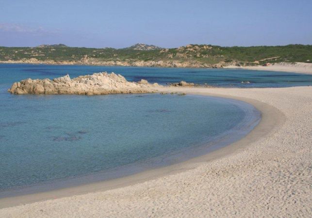 Spiaggia sabbiosa con mare azzurro e scogliere in lontananza.