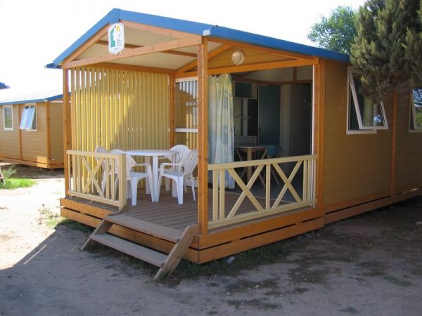 Chalet in legno con veranda e sedie bianche su una terrazza.