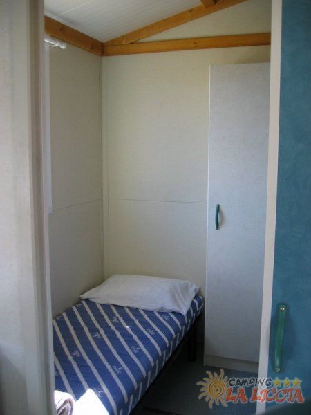 Letto singolo con lenzuola a righe blu e bianche vicino a un armadio.