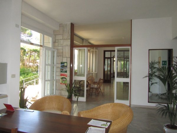 Sala luminosa con tavolo e poltrone, vista su porte aperte verso l'esterno.