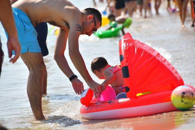 Adulto assistendo un bambino in un gonfiabile al mare.
