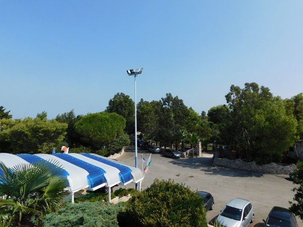 Strada con alberi e parcheggio, tetto blu e bianco visibile.