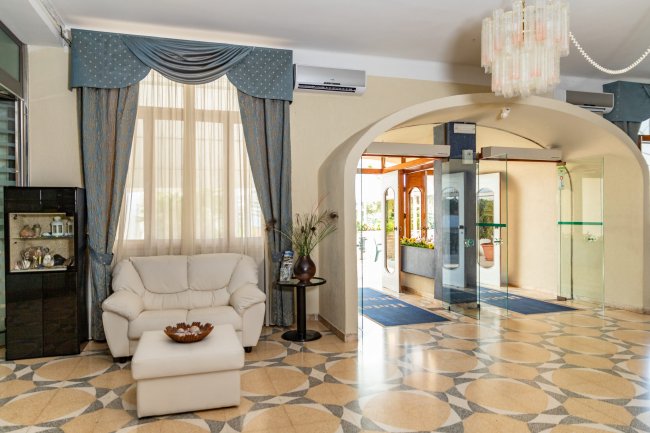 Sala d'ingresso con divano, tende blu e lampadario.