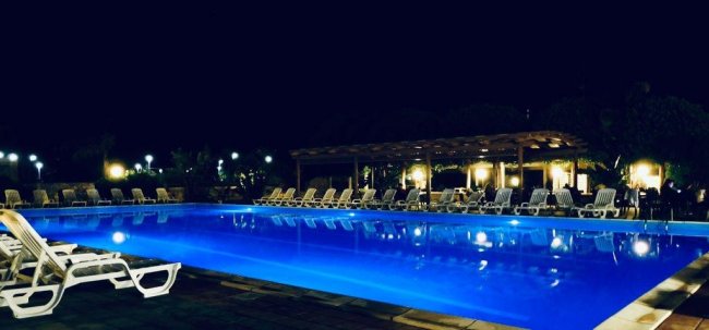 Piscina illuminata di notte con lettini attorno.