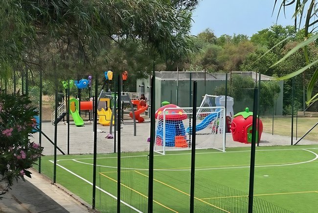 Campo sportivo con rete da calcio e parco giochi colorato recintato.