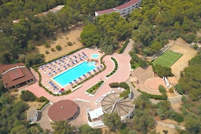 Vista aerea di un complesso con piscina, ombrelloni e anfiteatro.