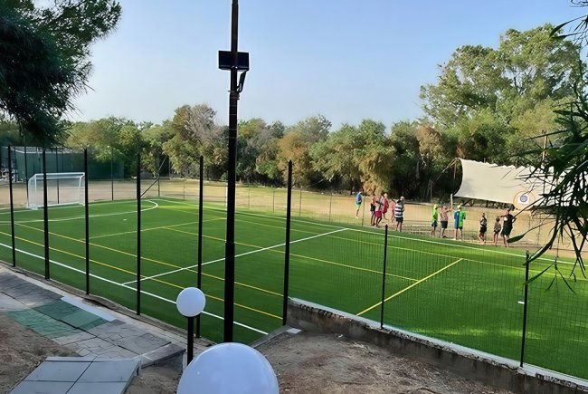 Un campo da calcio all'aperto con recinzione e un gruppo di persone lungo la linea laterale.