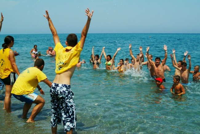 Persone che giocano e si divertono in mare, alcune indossano magliette gialle.