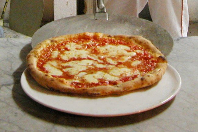 Pizza margherita su un piatto bianco appoggiato su un tavolo di marmo.