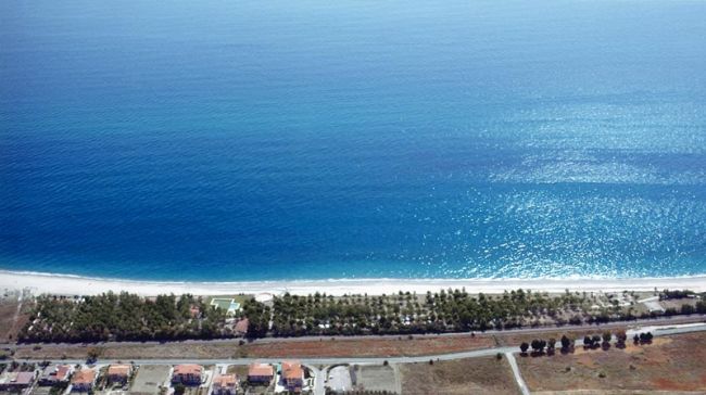 Vista aerea di una spiaggia con acqua blu e edifici residenziali sulla costa.