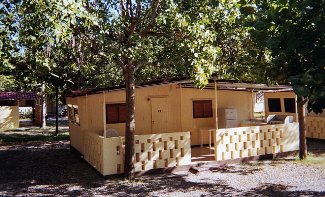 Una piccola casa gialla con veranda, immersa tra gli alberi.