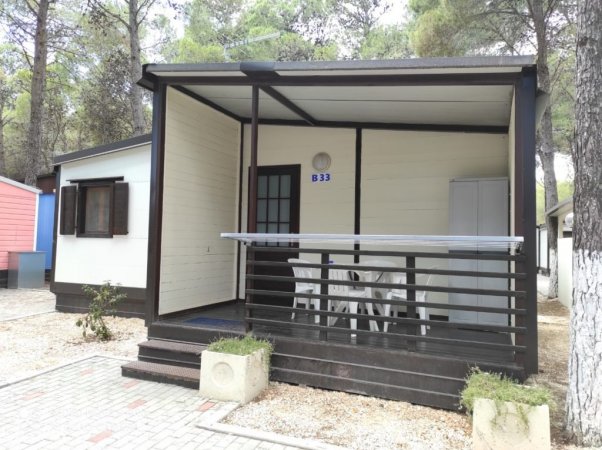 Bungalow con veranda coperta, tavolo e sedie bianche.