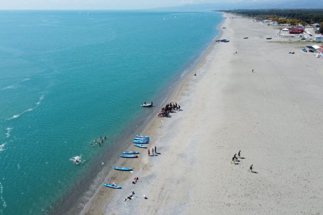 Lunga spiaggia con canoe e persone sul bagnasciuga.