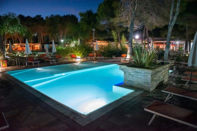 Piscina notturna con lettini e ombrelloni.