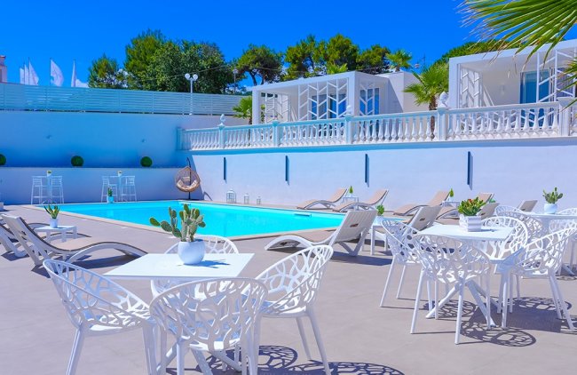 Piscina con lettini e tavolini bianchi.